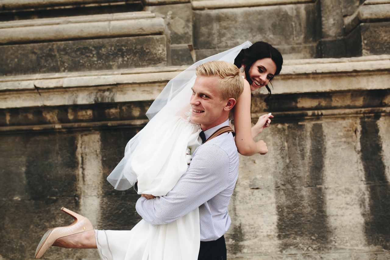 groom carries his bride in his arms through the old town
